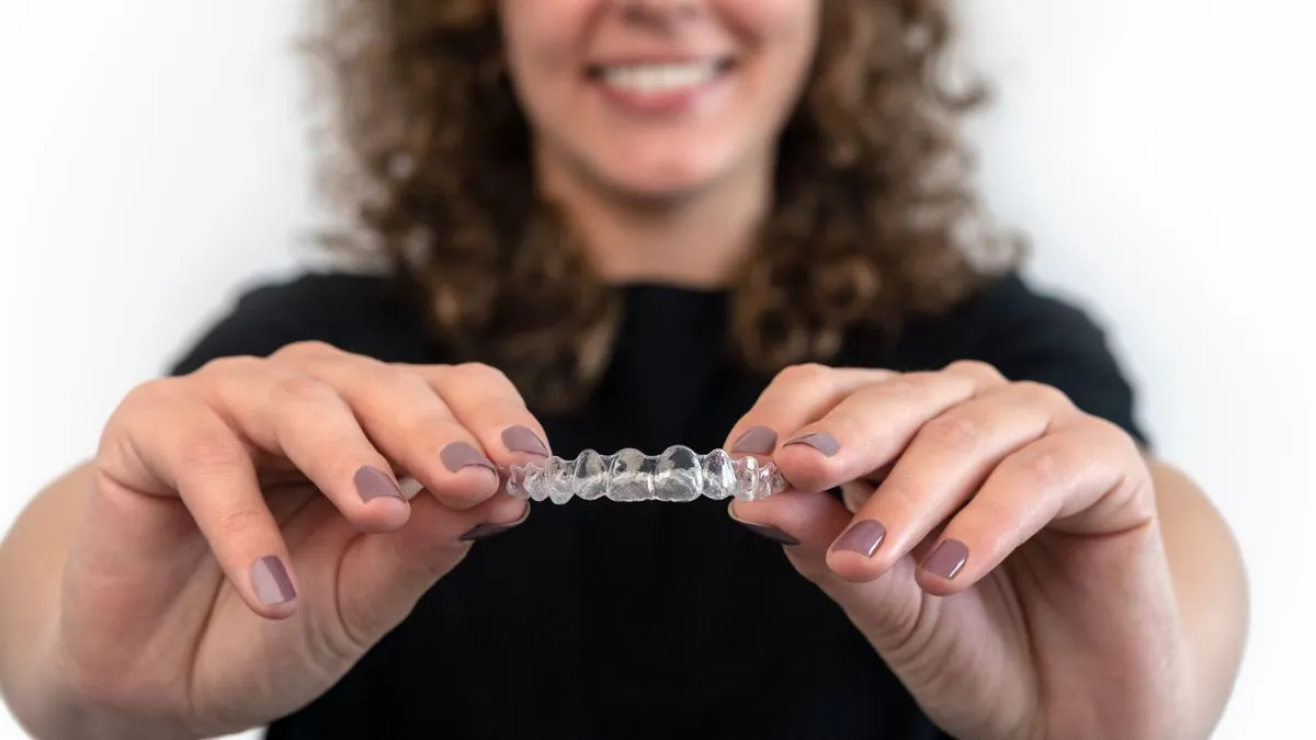 A clear dental aligner held in front of a smiling patient