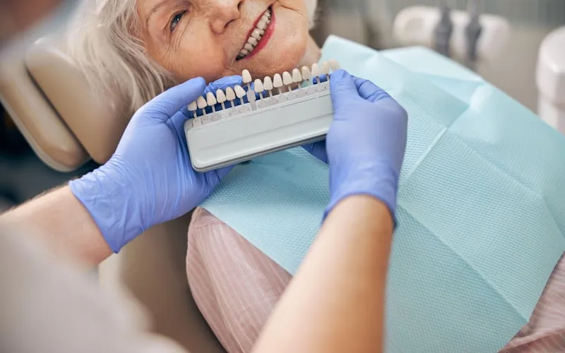 Dentist comparing a porcelain shade guide to a patient's natural teeth